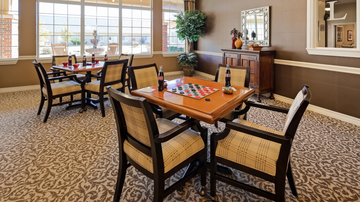 A cozy interior room featuring a game table with chairs, decorative elements, and large windows.