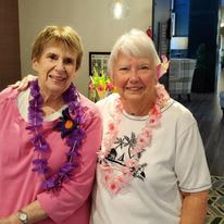 Two women smiling indoors, each wearing a lei.