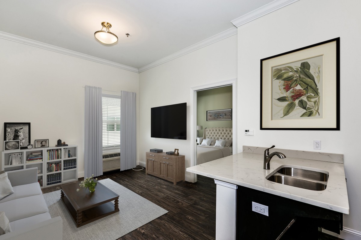 A modern, open-concept living room with a TV, coffee table, and kitchen counter.