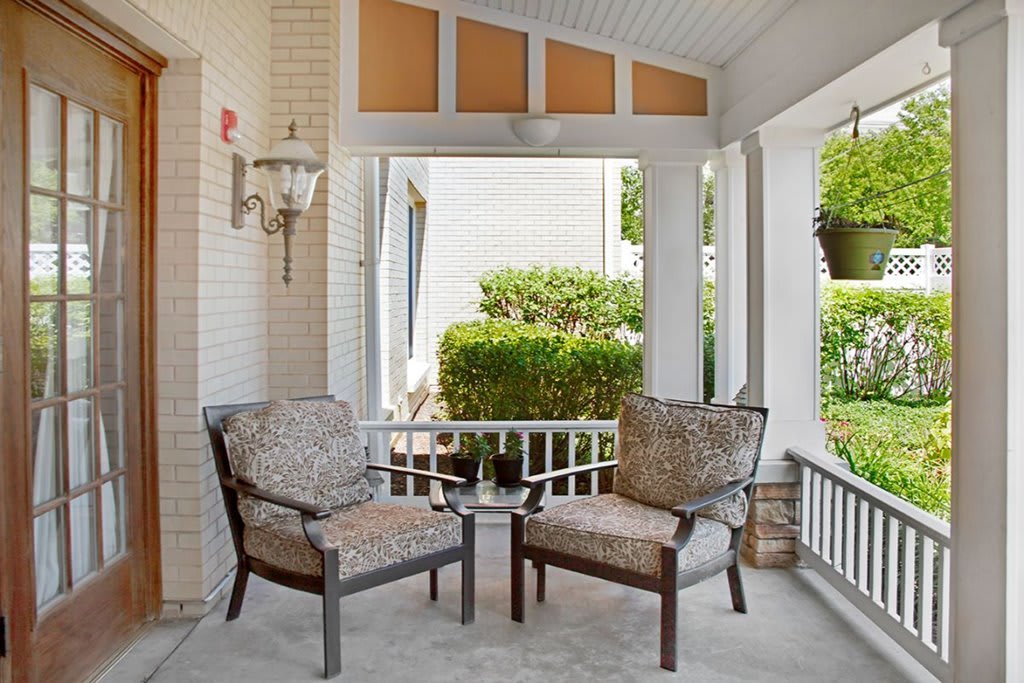 A cozy porch with two comfortable chairs and lush greenery creates a perfect relaxation spot.