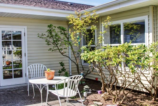 A sunlit patio with white metal furniture and surrounding greenery.