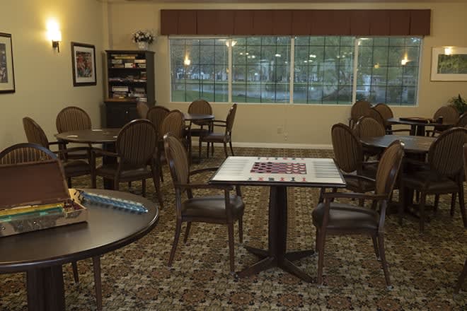 A cozy game room with tables and chairs, featuring a checkerboard and books in the corner.