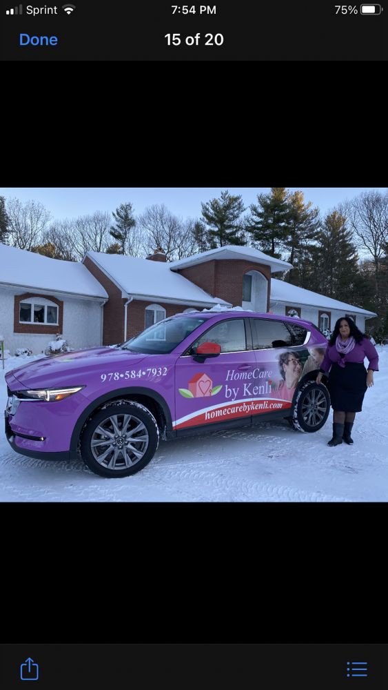 A woman stands next to a purple car with advertising graphics in a snowy outdoor setting.