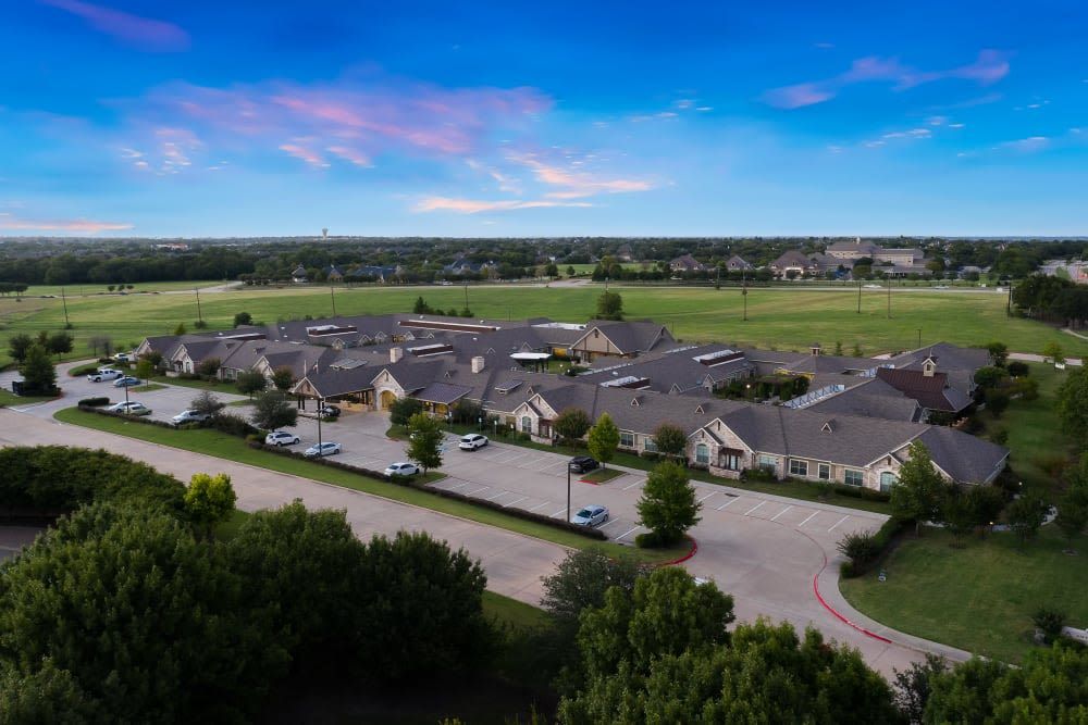 Aerial view of a suburban residential area with rows of houses and surrounding greenery under a blue sky.