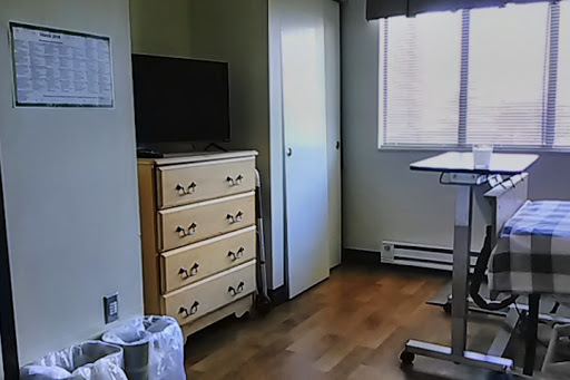 A simple hospital room featuring a television, dresser, and a view out the window.
