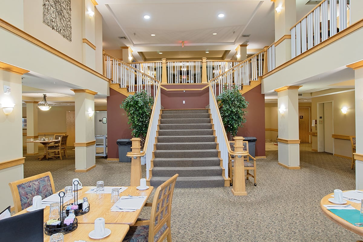 A spacious hotel lobby featuring a grand staircase and a dining area.