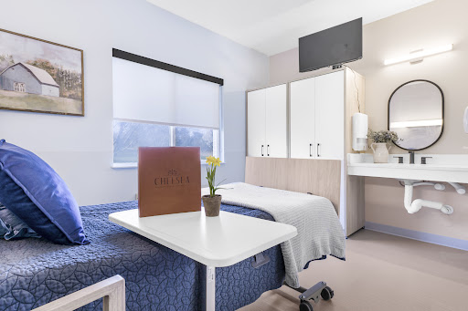 A well-furnished hospital patient room featuring two beds, a small table, and modern amenities.