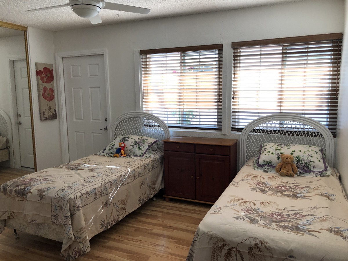 A cozy bedroom featuring two twin beds with floral bedspreads, wooden flooring, and window blinds.