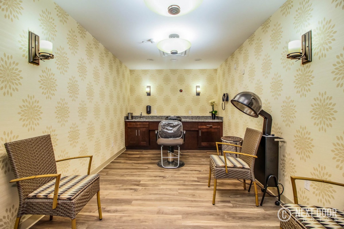 A vintage-themed salon with a barber chair, hair dryer, and waiting area seating.