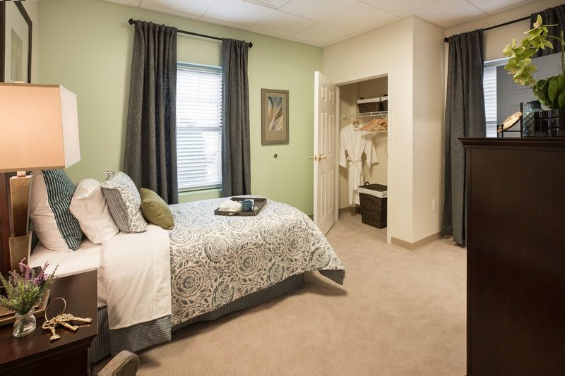A cozy bedroom with green walls, featuring a bed, curtains, and an open closet.