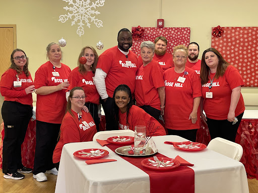 A cheerful group of volunteers posing together during a holiday celebration, showcasing their festive spirit with red shirts and a beautifully set table.