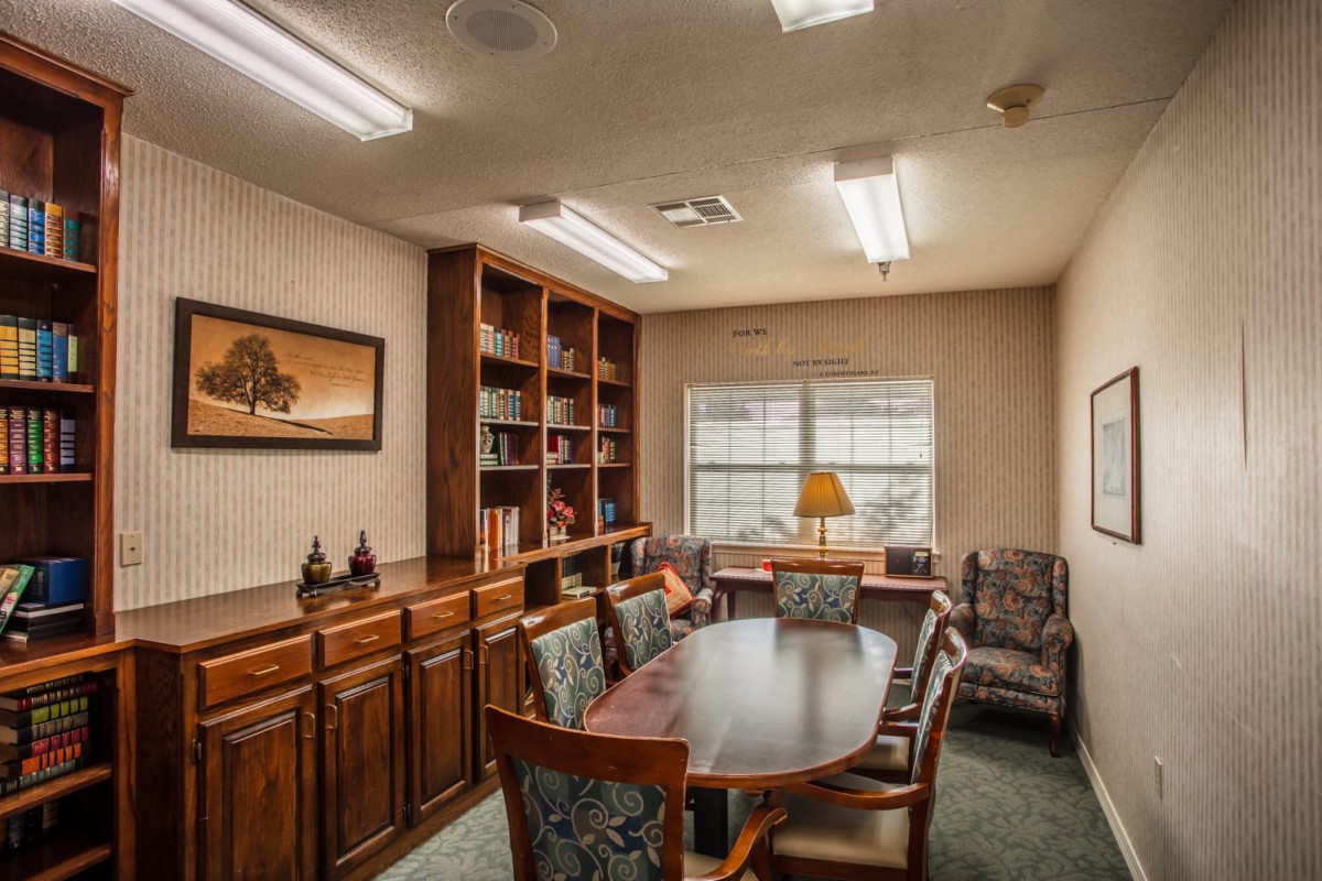 A small office meeting room with a table, several chairs, and a bookshelf.