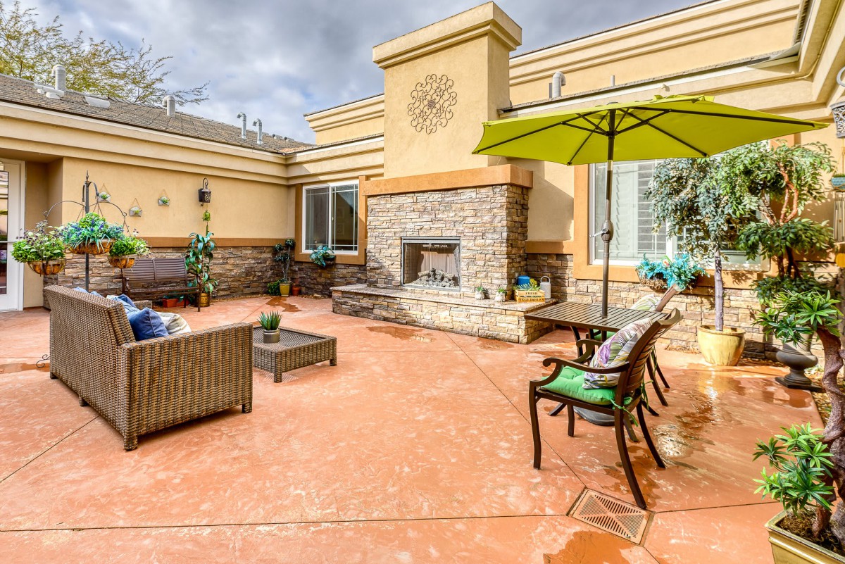 A cozy outdoor patio with comfortable seating, a stone fireplace, and a large umbrella.