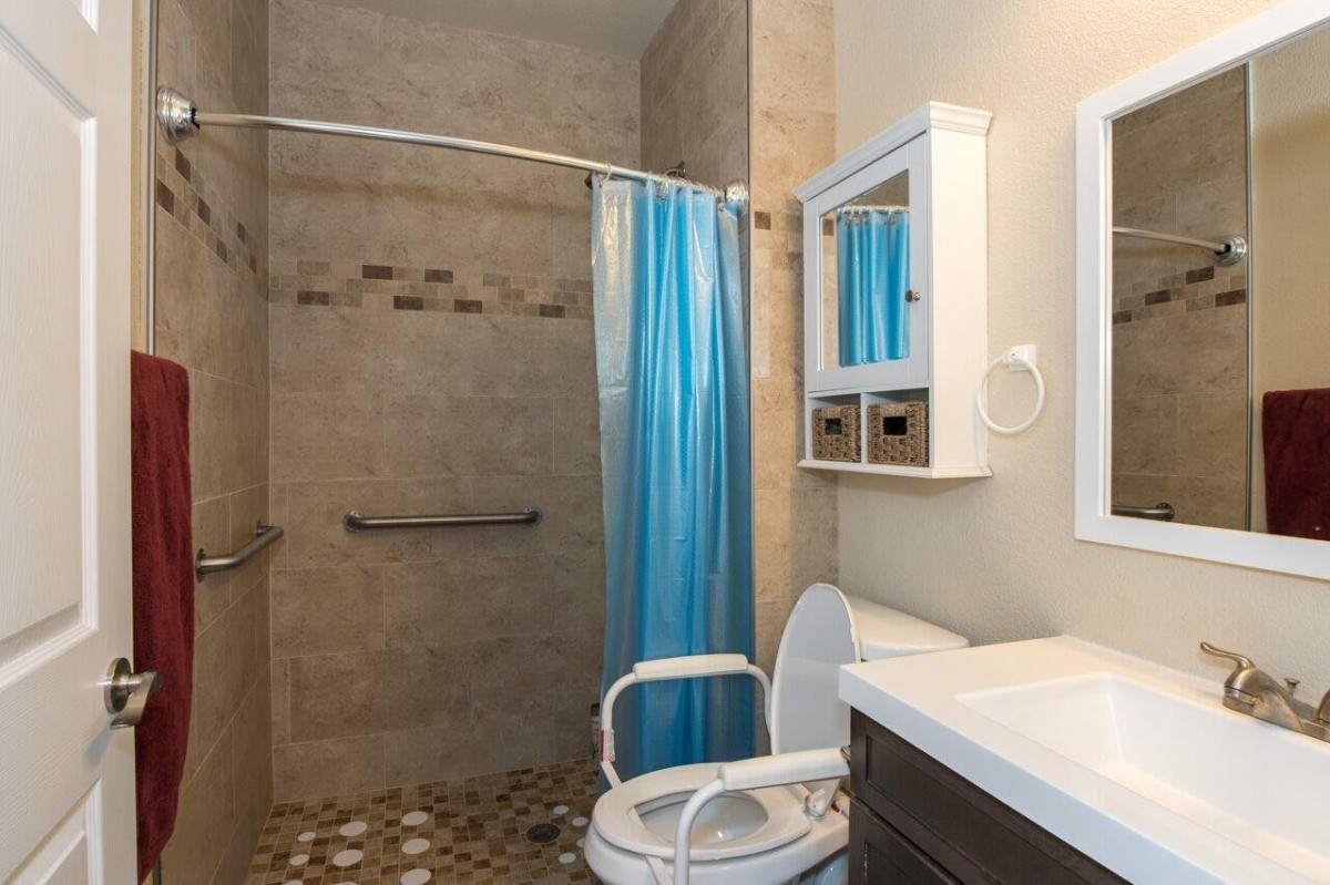A wheelchair-accessible bathroom with a blue shower curtain and tiled walls.