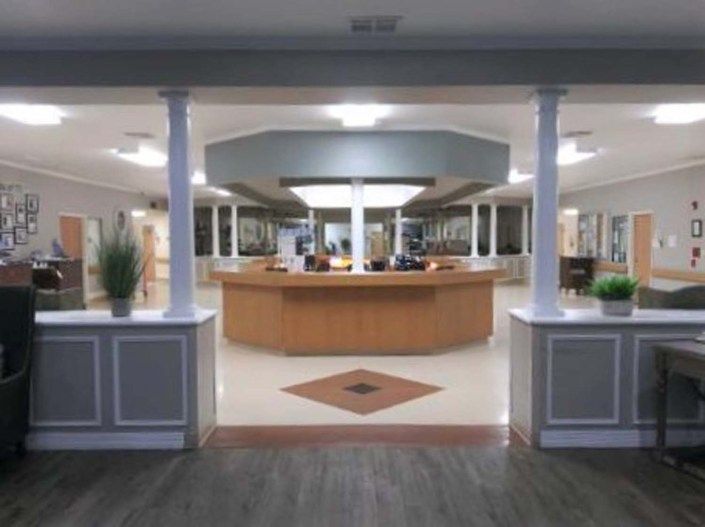 A spacious and modern reception area featuring a central wooden desk, surrounded by decorative columns and potted plants.