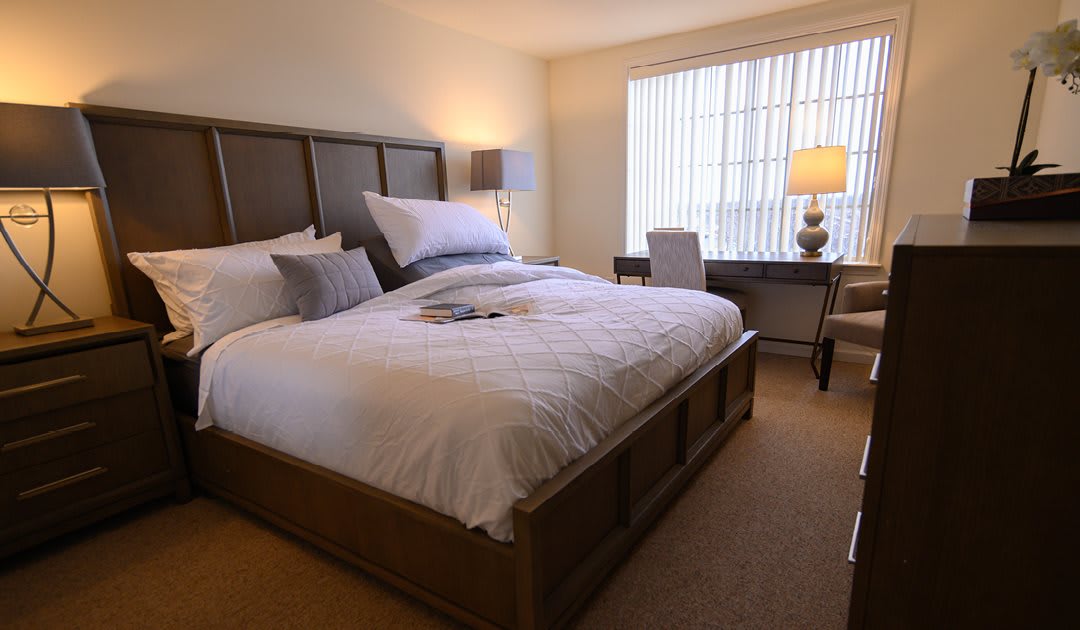 A cozy bedroom with a large bed, a desk, and soft lighting.