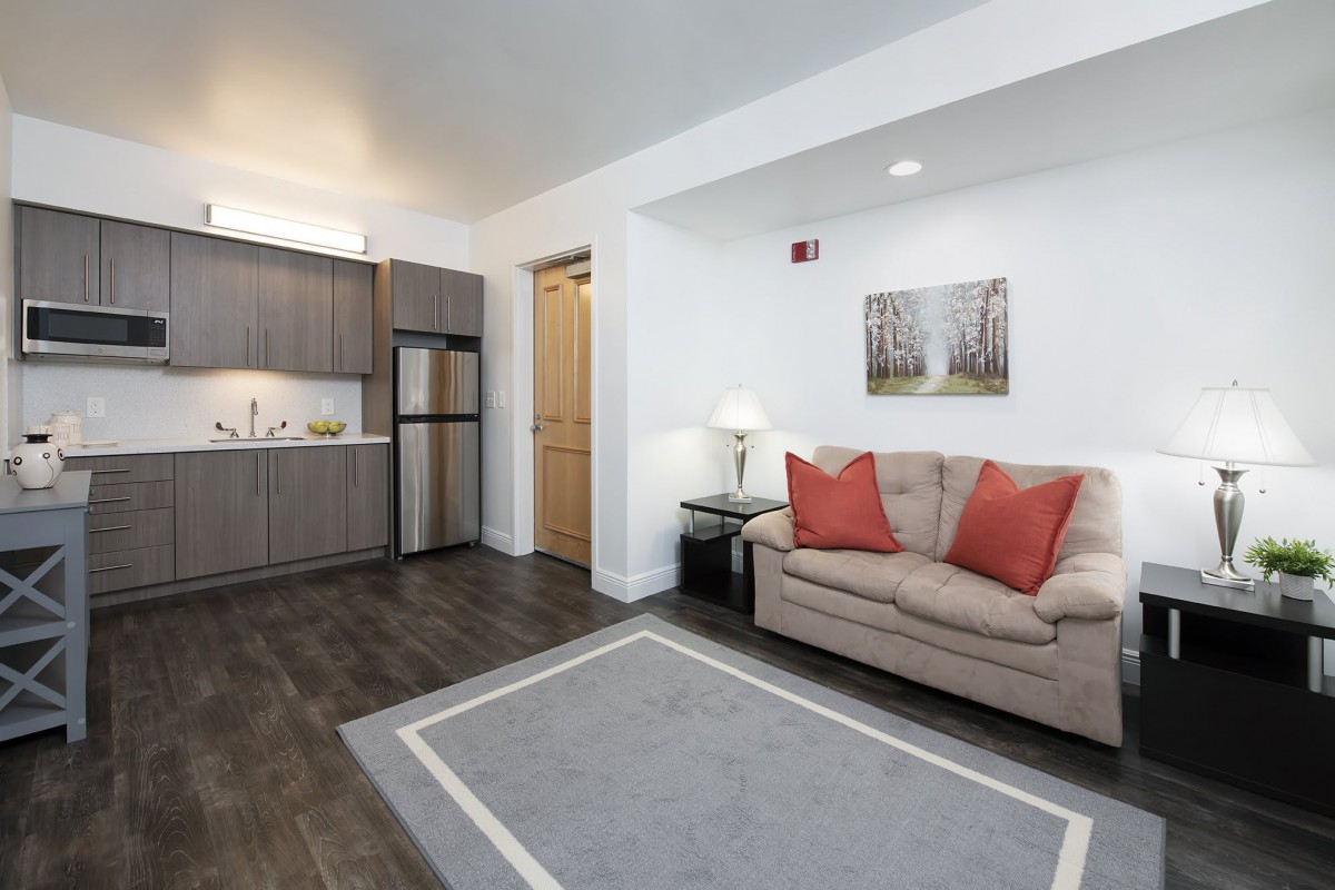 A modern apartment living area featuring a compact kitchen and a cozy sofa with red cushions.