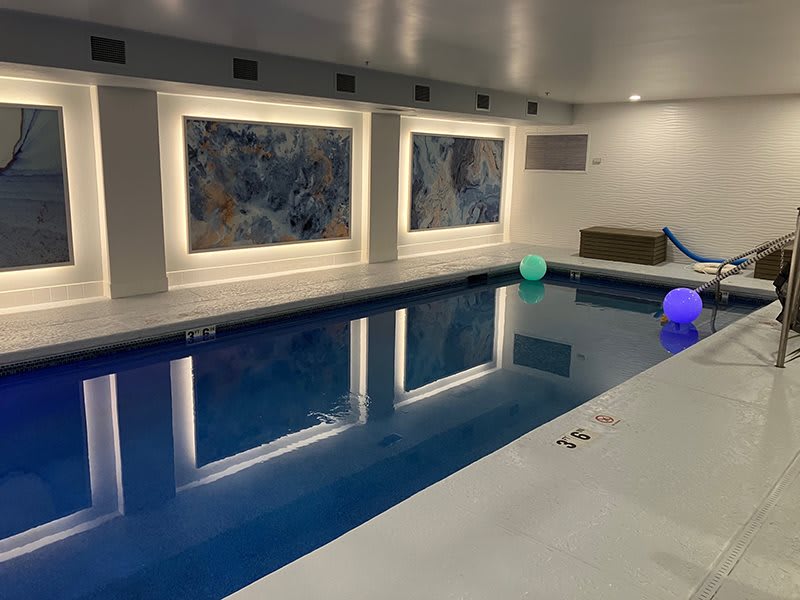 A modern indoor swimming pool with colorful lighting and wall art.