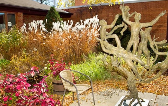 An outdoor garden featuring a unique sculpture surrounded by autumn foliage and a solitary chair.