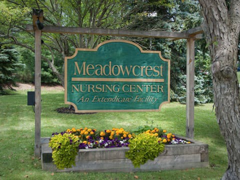 A sign for Meadowcrest Nursing Center surrounded by a landscaped garden with colorful flowers.