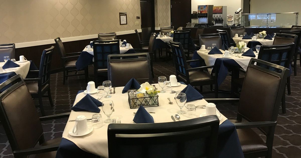 Elegantly set tables in a restaurant dining area, featuring white tablecloths and navy blue napkins.