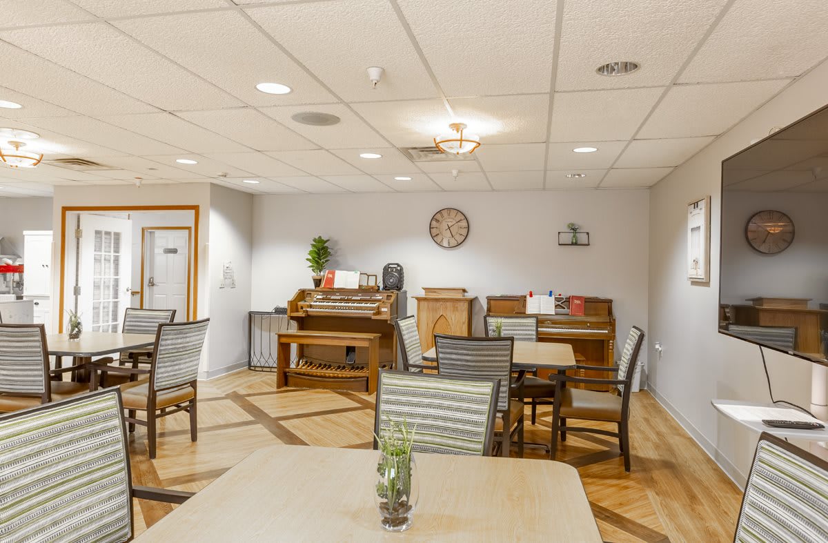 A cozy indoor dining area with tables, chairs, and a piano against the wall.
