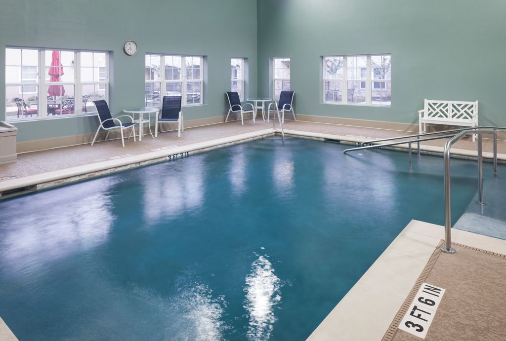 An indoor swimming pool area with tables and chairs by the windows.