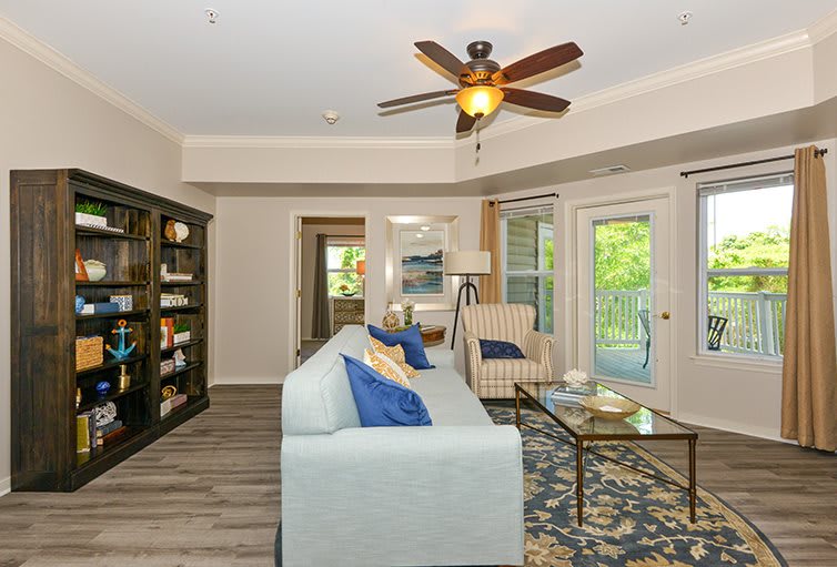 A cozy living room with modern decor, featuring a ceiling fan, sofa, armchair, and a bookshelf.