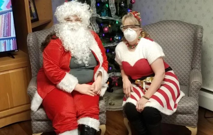 Two people dressed in festive Christmas costumes sitting indoors.