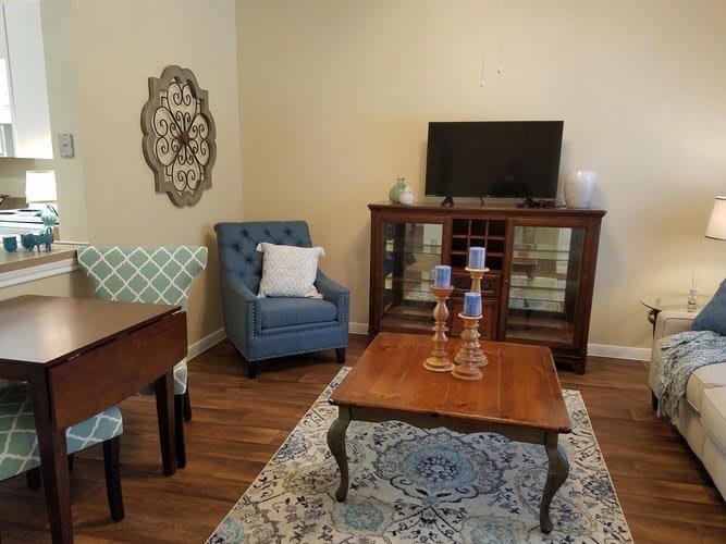 A cozy living room with a blue armchair, wooden coffee table, and a cabinet with a television.