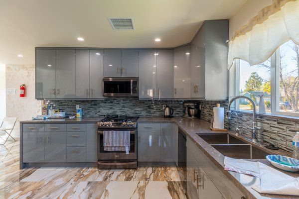A modern kitchen with gray cabinets, a sleek backsplash, and marble flooring.