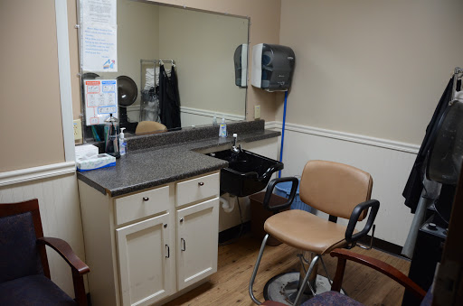 A view of a hair salon space featuring a chair, mirror, and sink.