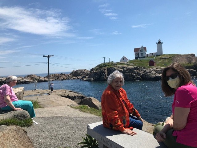 A woman sitting by the water with a lighthouse in the background on a sunny day.