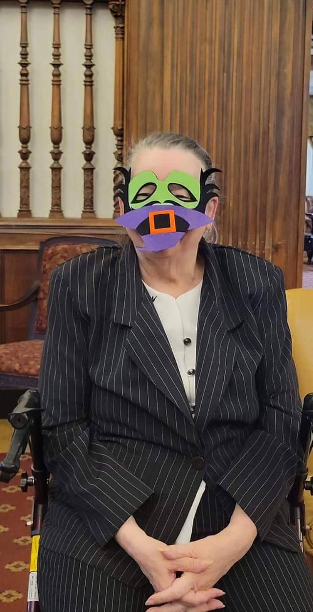 A person in formal attire wearing a colorful mask at an indoor event.