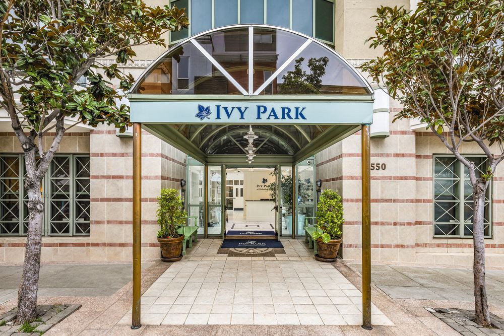 The entrance to a building named Ivy Park, featuring a covered walkway and potted plants on either side.
