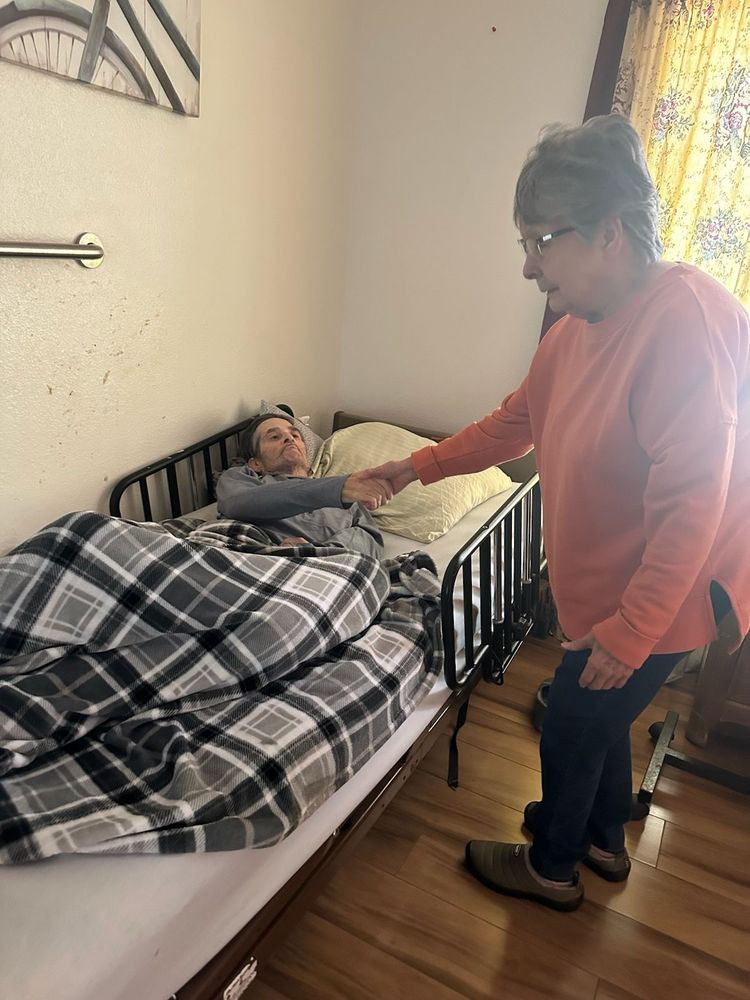 A person standing beside a bedridden individual, offering care and support.