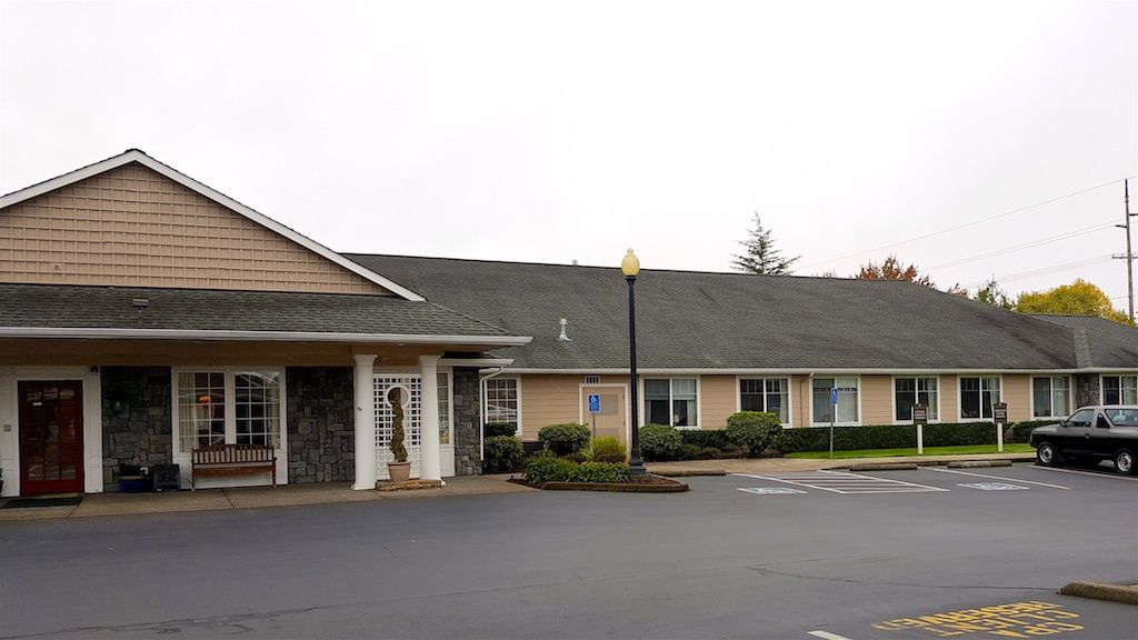 A single-story building with a parking lot in front, featuring a lamppost and some landscaping.