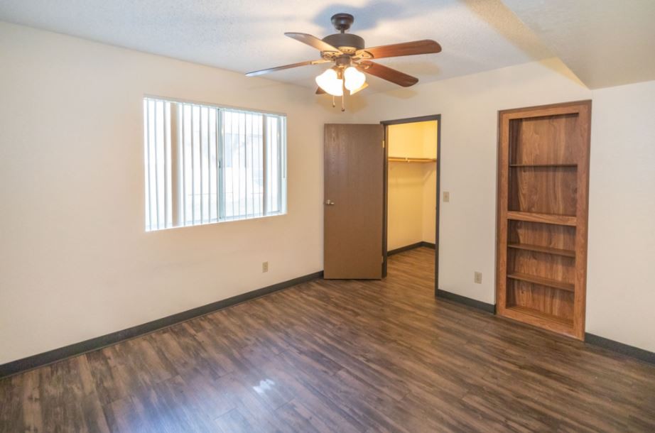 An empty room with a ceiling fan, wooden floor, and built-in shelves.