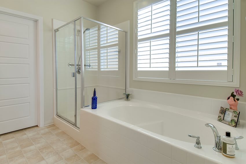 A modern bathroom with a bathtub and glass-enclosed shower next to windows with shutters.