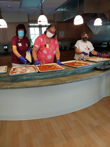 Healthcare workers preparing food in a kitchen setting, demonstrating safety protocols with masks and gloves.