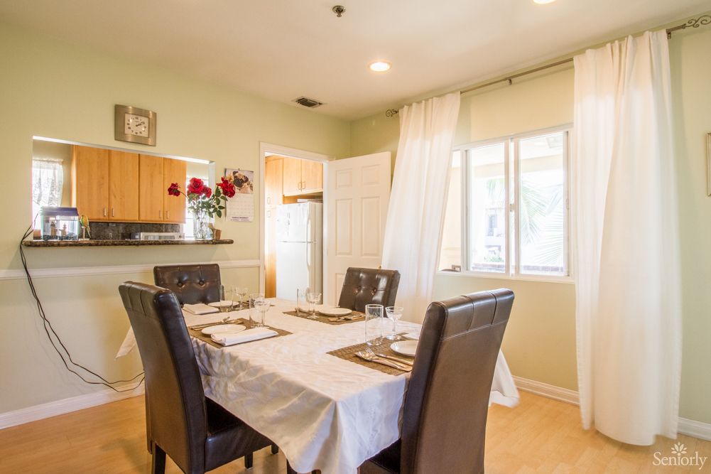 A well-lit dining room featuring a table set for four with a view into the adjacent kitchen.