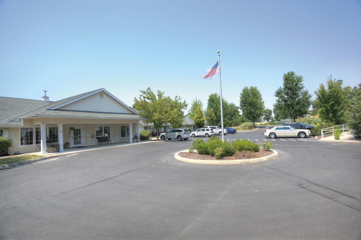 A single-story building with a flagpole, surrounded by a landscaped parking lot and several parked cars.