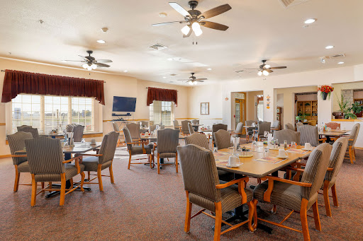 A spacious dining area with neatly arranged tables and chairs, featuring ceiling fans and warm lighting.