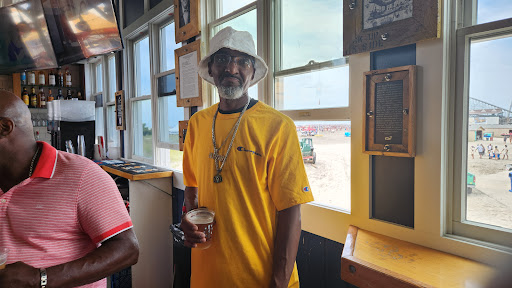 A man enjoying a drink while dressed in a vibrant yellow shirt and bucket hat, standing by the window.