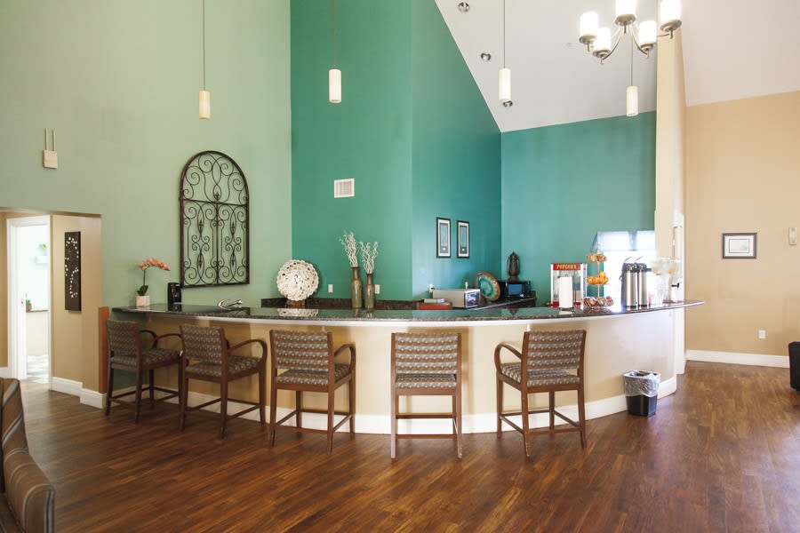 A cozy reception area with a wooden floor and green walls, featuring a counter with chairs and decorative items.