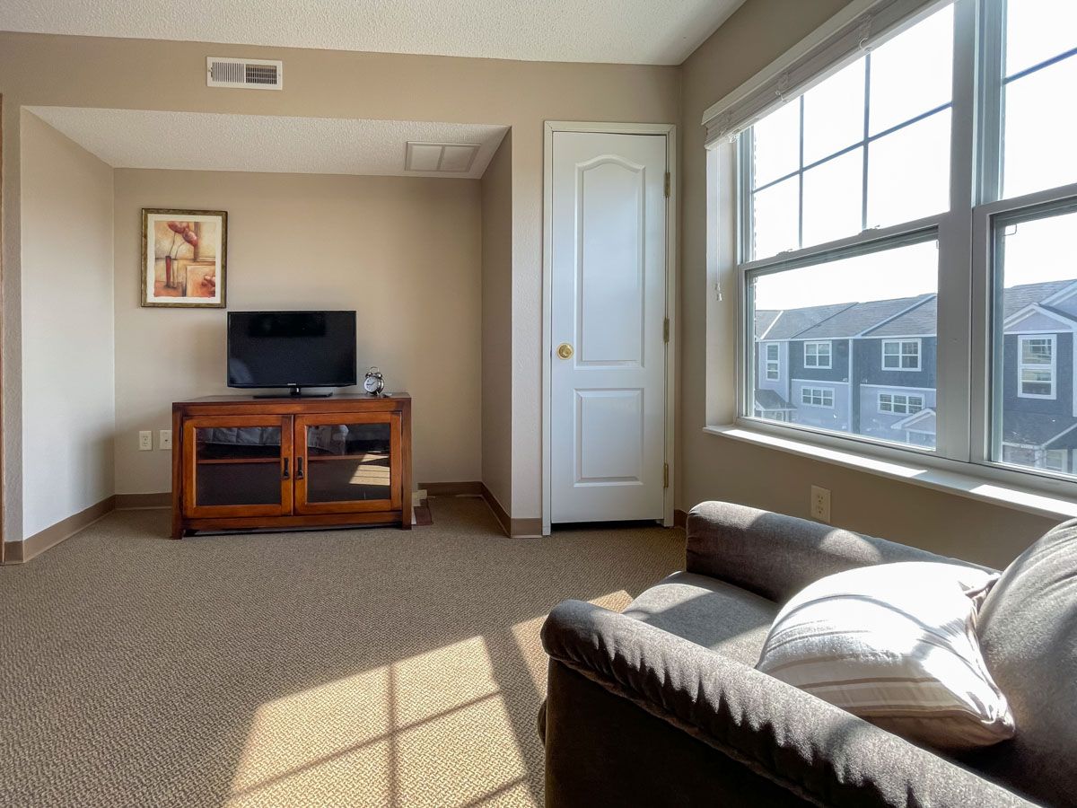 A cozy living room with a television, sofa, and large window letting in sunlight.