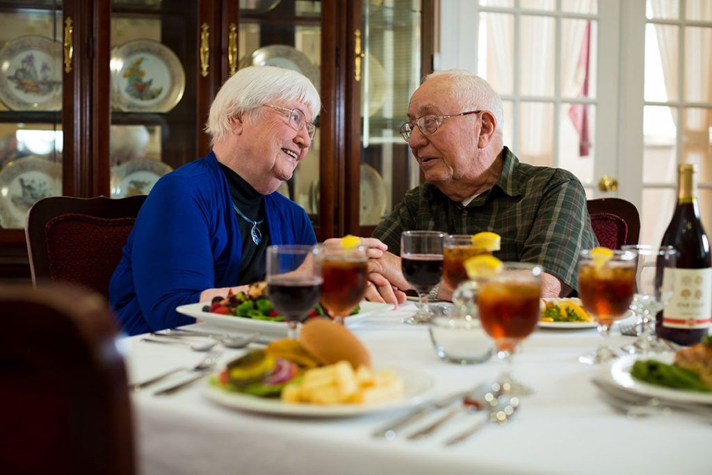 An elderly couple enjoying a meal together, sharing laughter and holding hands.