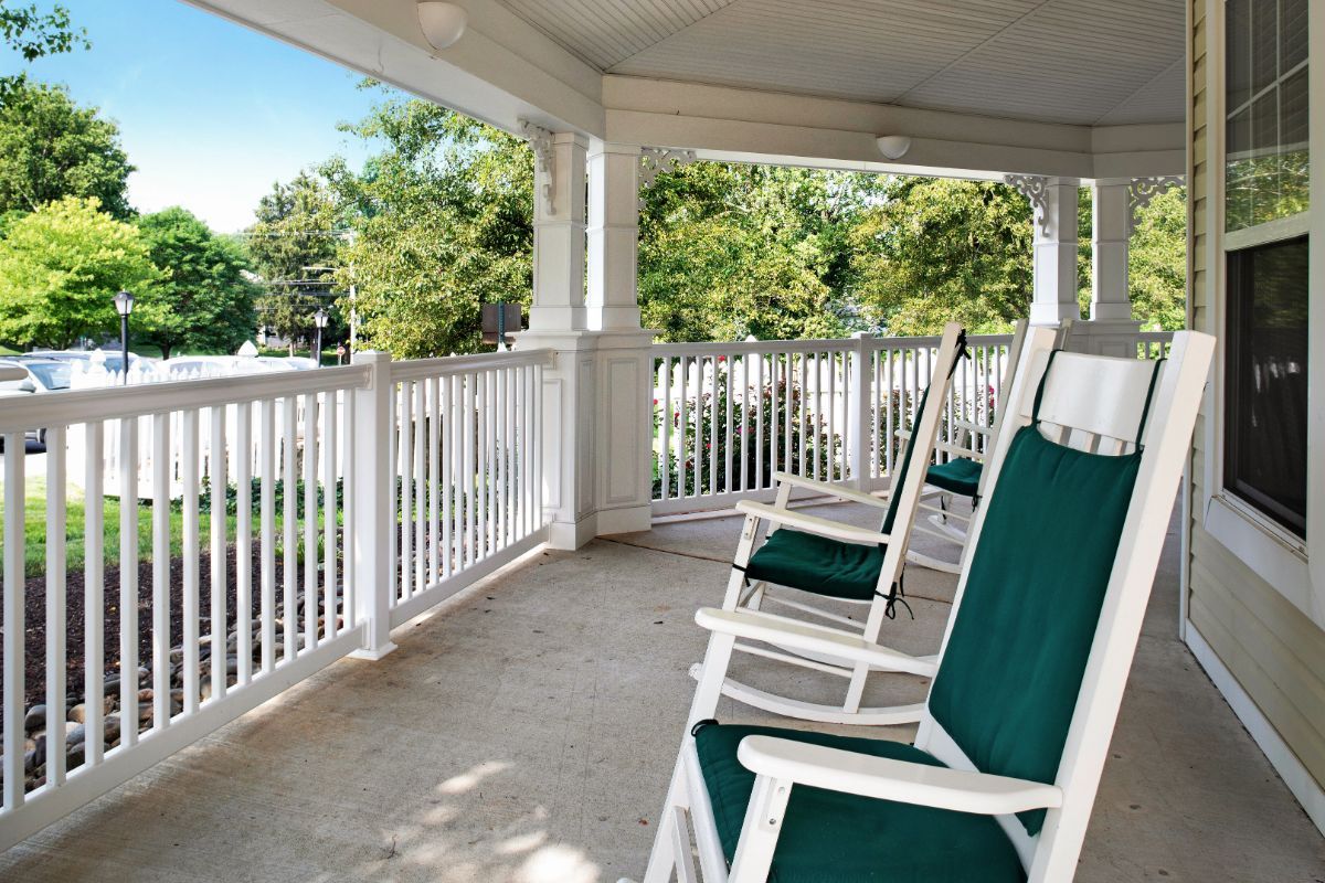 A peaceful porch with green-cushioned rocking chairs overlooking a sunny garden.
