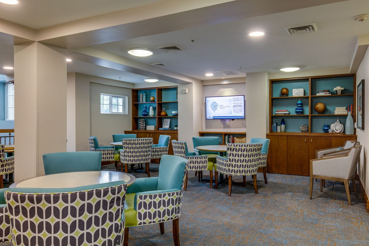 A cozy lounge area with patterned chairs and tables, featuring a television and bookshelves.