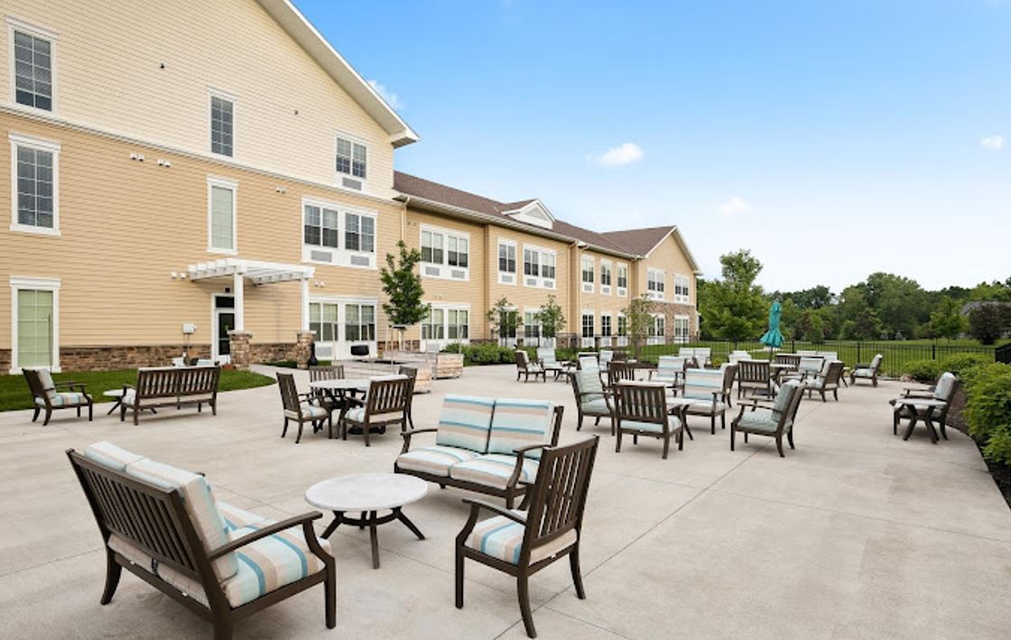 An outdoor patio area with seating arrangements in front of a large residential building on a sunny day.